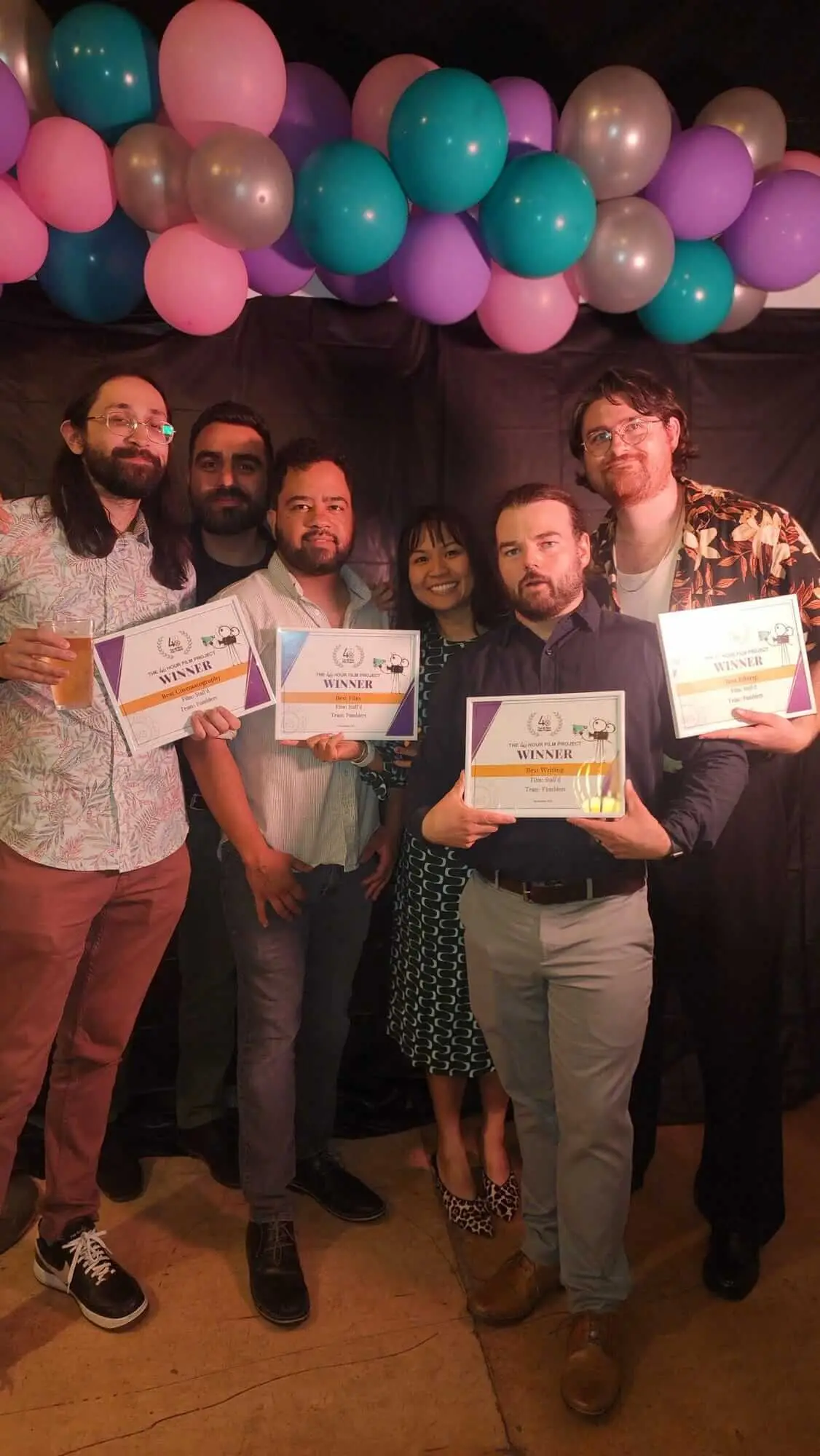 Six guests pose together holding framed film awards