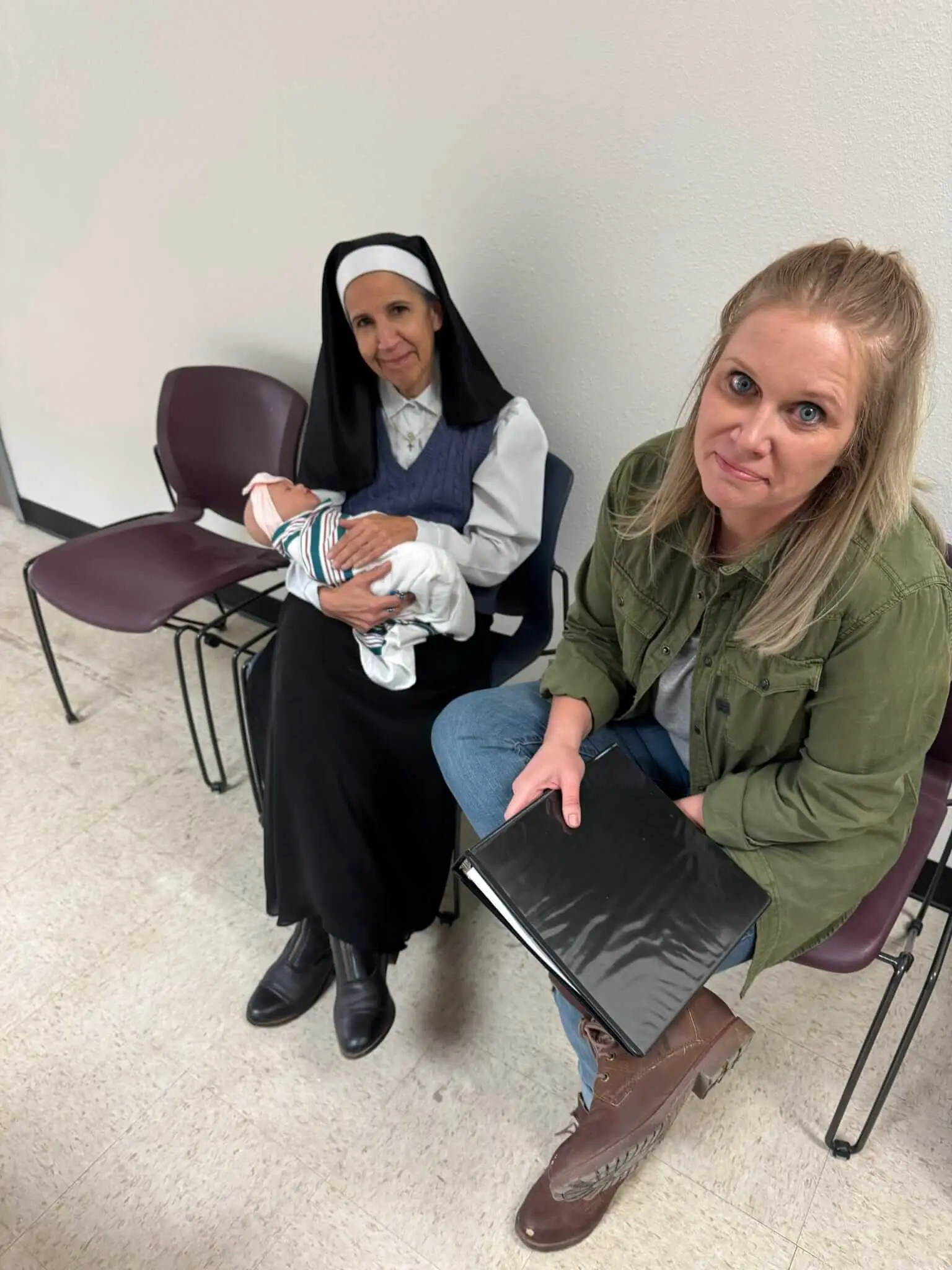 A performer dressed as a nun holds a baby prop beside a crew member