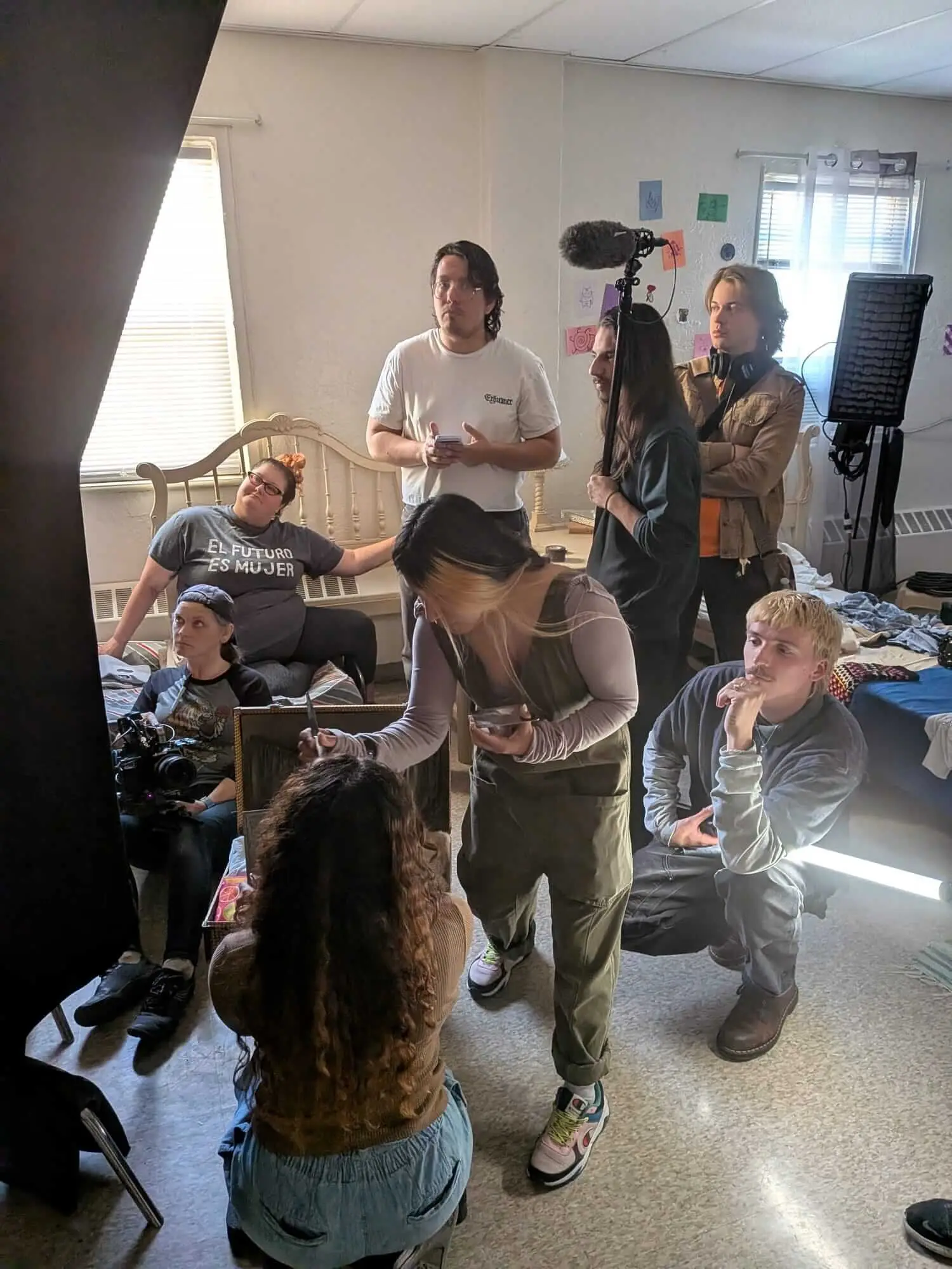 Cast and crew prepare a bedroom scene around lights and camera equipment