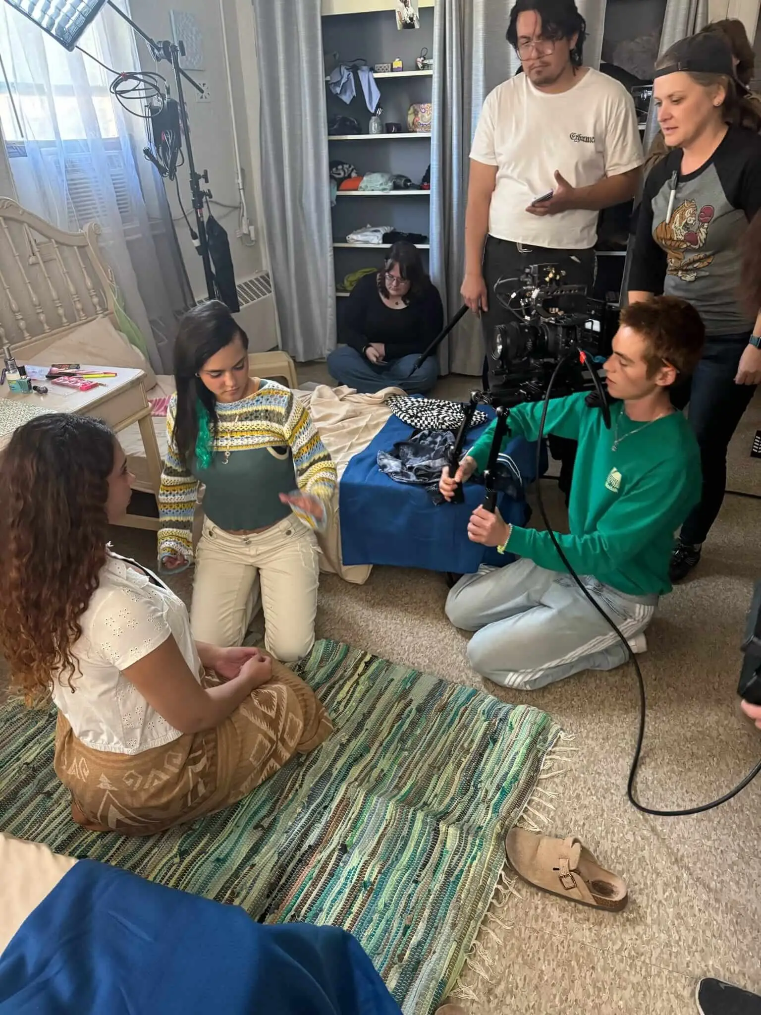 Cast and crew frame a bedroom scene around a camera rig